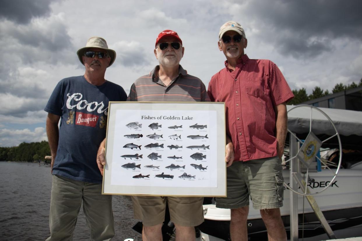 From left to right, Jay Foran, Peter Heinermann and Don Bishop pose with an illustration of several of the fish species that call Golden Lake home. They've hatched a plan to return the population of walleye in the eastern Ontario lake to numbers not seen in decades. (Trevor Pritchard/CBC - image credit)