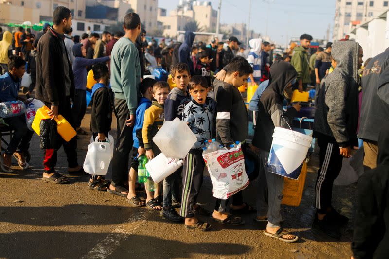 Palestinian children queue as they wait to collect drinking water, amid shortages of drinking water, as the conflict between Israel and Hamas continues, in Rafah