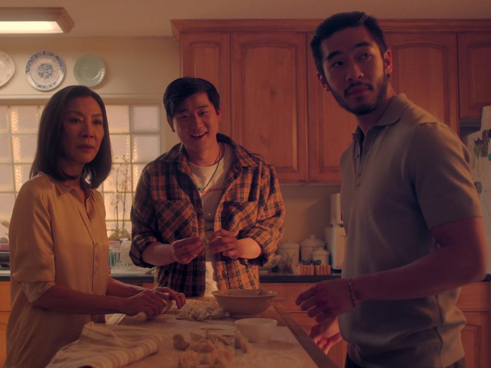 mama sun, bruce sun, and charles sun in the brothers sun, standing around a kitchen island making dumplings