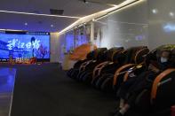 A man wearing a mask sits in a massage chair near a screen showing a trailer for the film "Days and Nights in Wuhan" outside a mall in Wuhan in central China's Hubei province on Friday, Jan. 22, 2021. China is rolling out the state-backed film praising Wuhan ahead of the anniversary of the 76-day lockdown in the central Chinese city where the coronavirus was first detected. (AP Photo/Ng Han Guan)