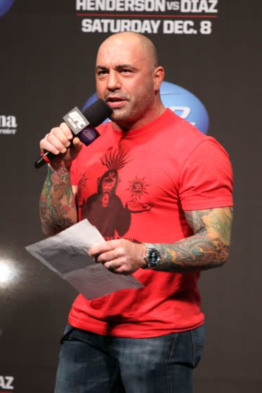 A bald man wearing a read T-shirt and arm tattoos speaking into a microphone