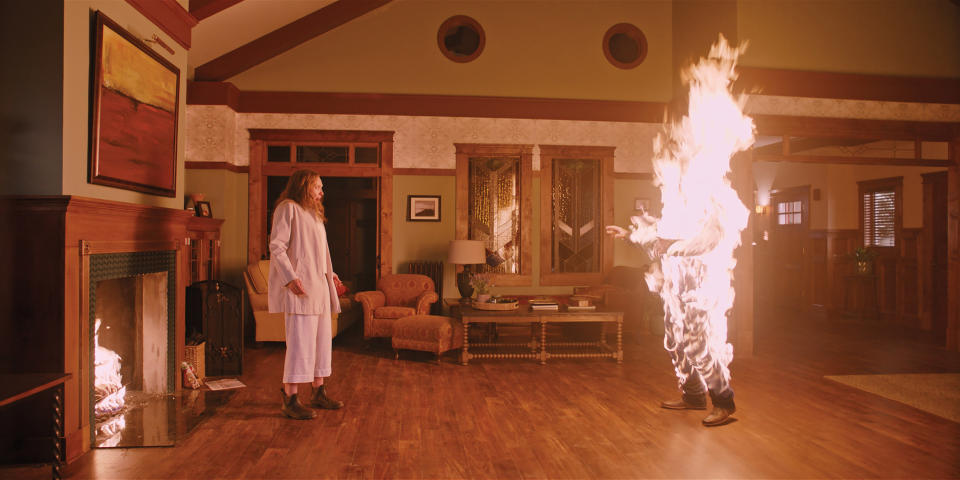 A person on fire looking at another person inside a house