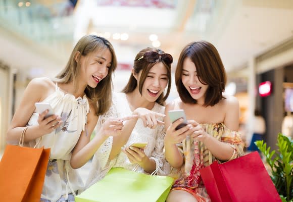 Three smiling young shoppers using their smartphones.