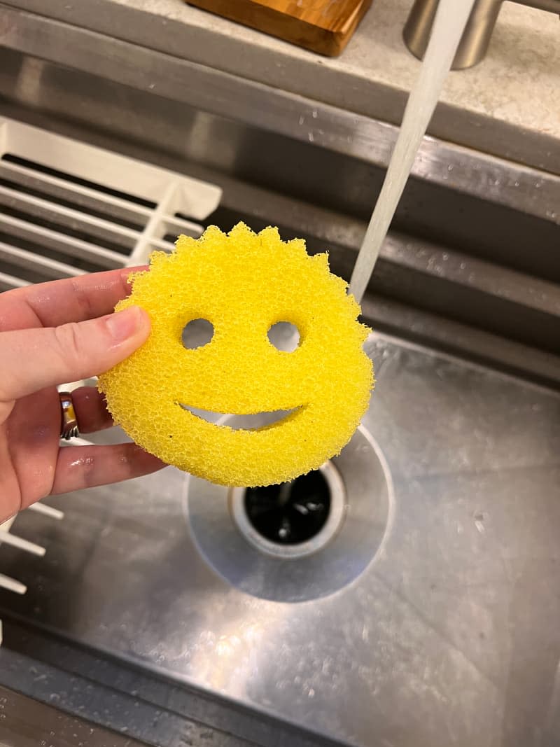 Someone holding sponge above the sink.