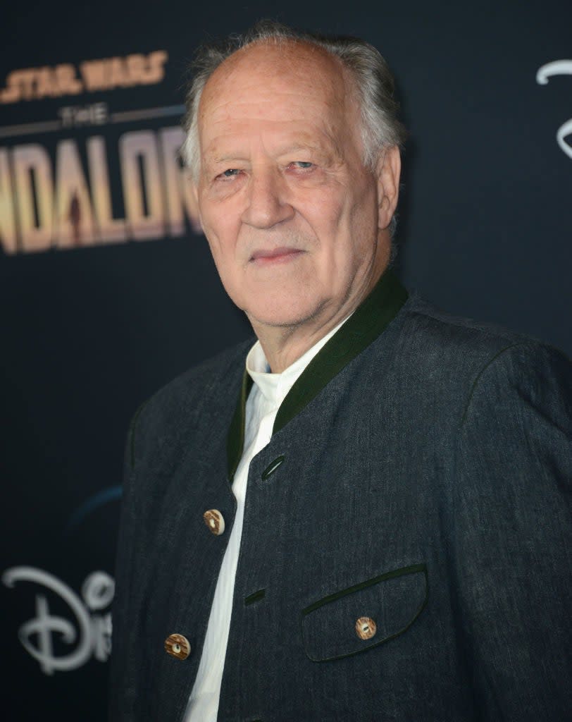 Man in a grey jacket and white shirt posing at 'The Mandalorian' event