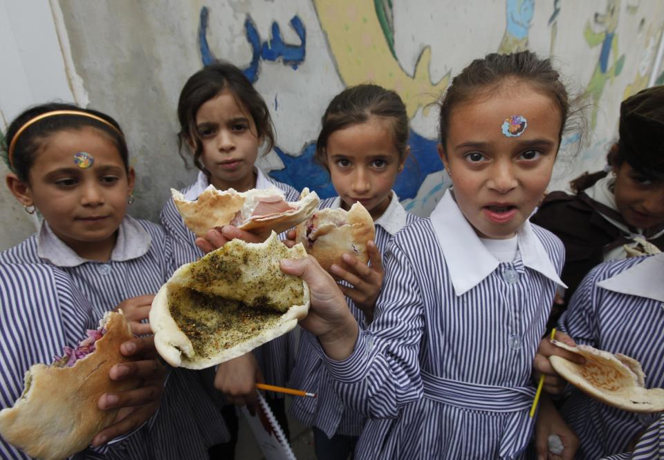 Palestinian students hold up their sandwiches of pita bread stuffed with olive oil and zaatar, a mixture of herbs and spices, brought from home, during their half-hour mid-day break at about 11 a.m. in the West Bank city of Nablus, Tuesday, May 6, 2014. Palestinian children in the West Bank usually eat during recess in the schoolyard, as there are no dining rooms in schools. (AP Photo/Majdi Mohammed)