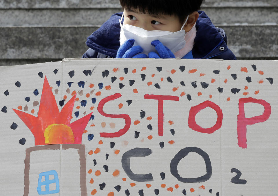 A boy wearing a mask sits behind a banner during a rally for global climate strike for future in Seoul, South Korea, Friday, March 15, 2019. About 150 students and other protesters attended a rally to protest their governments' failure to take sufficient action against climate change. (AP Photo/Lee Jin-man)