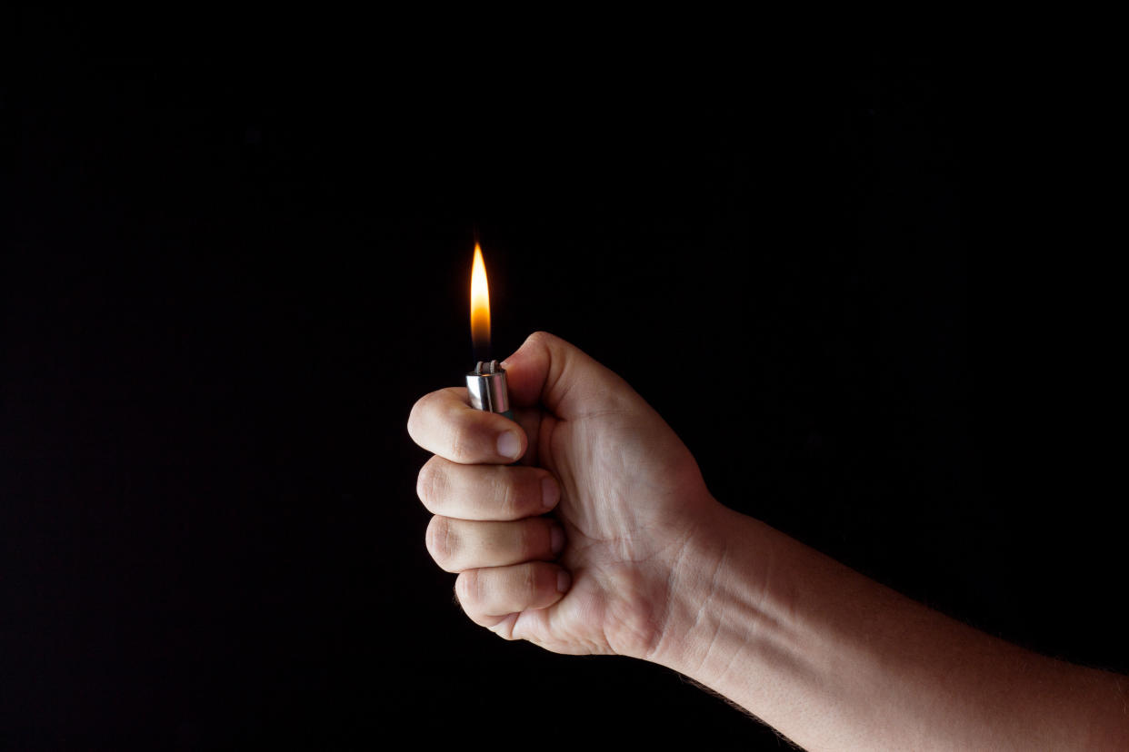 Cropped Hand Of Woman Igniting Cigarette Lighter Against Black Background