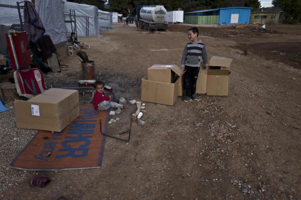A Syrian refugee child plays on the ground while a boy collects cardboard boxes at the refugee camp of Ritsona about 86 kilometers (53 miles) north of Athens, Thursday, Jan. 5, 2017. Over 62,000 refugees and migrants are stranded in Greece after a series of Balkan border closures and an European Union deal with Turkey to stop migrant flows. (AP Photo/Muhammed Muheisen)