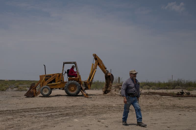 Ranger Briggs walks past as oil specialist Dunlap excavates well in Pecos County, Texas