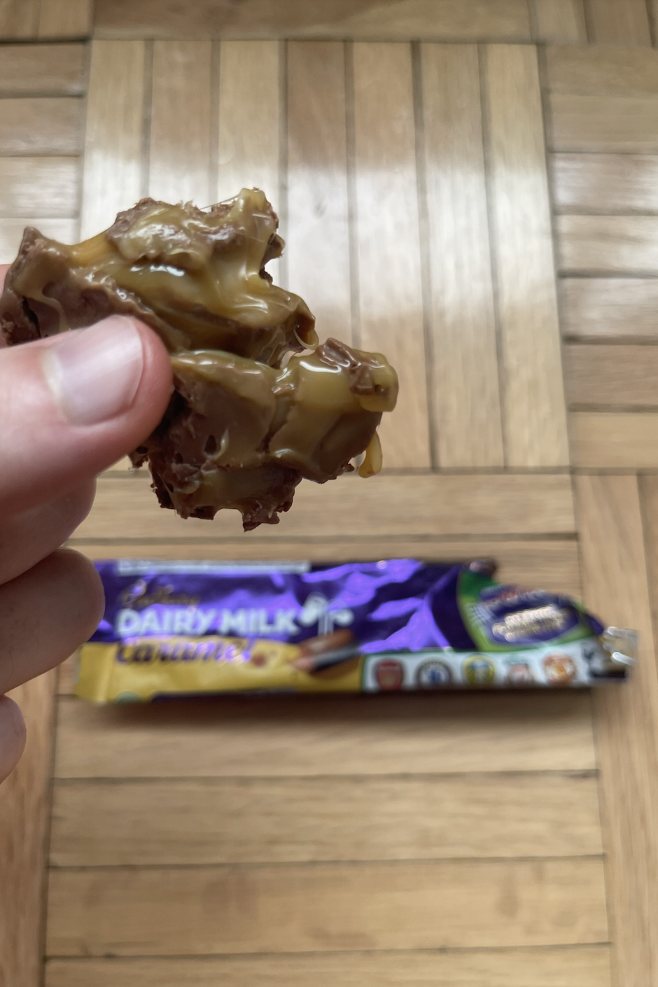 A hand holding a half-eaten chocolate bar with nuts, with an unopened bar of the same kind in the background
