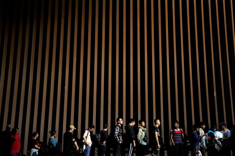 People line up against a border wall as they wait to apply for asylum after crossing the border from Mexico on July 11, 2023, near Yuma.