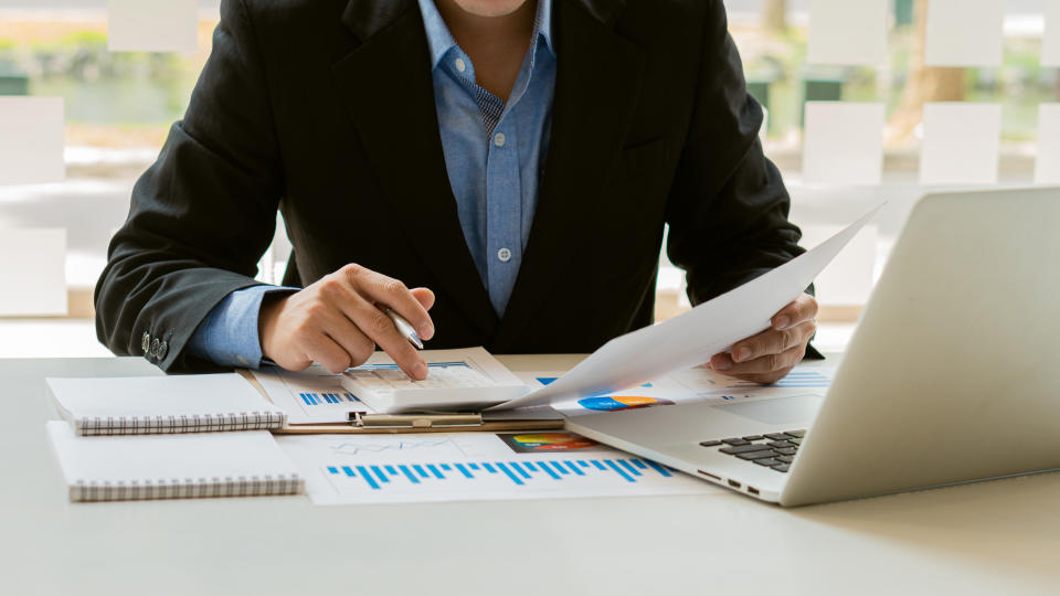 Hand pressing a calculator, analyzing financial documents while holding a pen in your finger. Young Asian businessman charging taxes, bills, credit card for payment, financial concept.