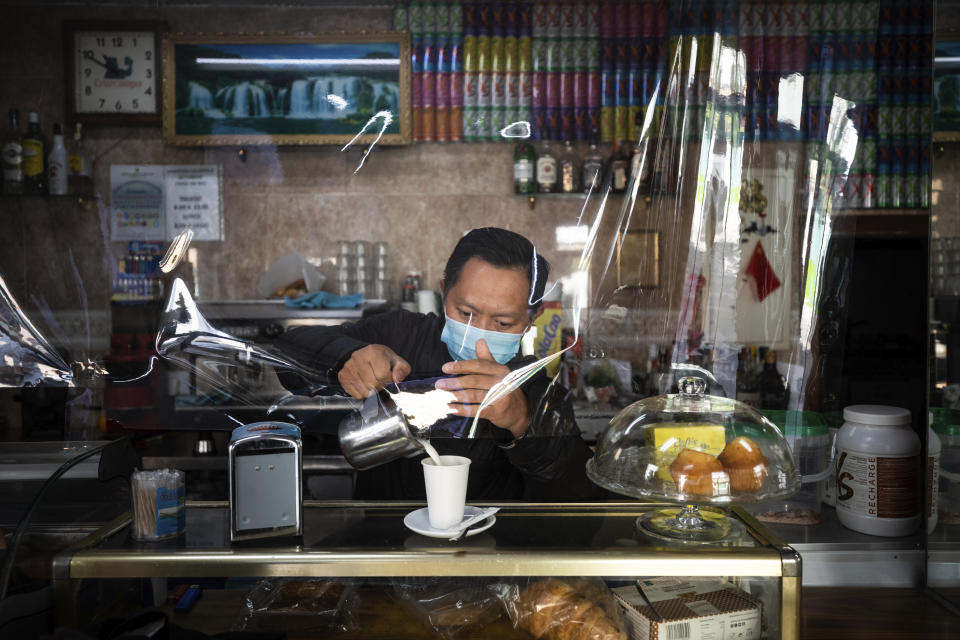 A waiter wearing a face mask and behind a plastic curtain to prevent the spread of coronavirus serves a coffee at a bar in the southern neighbourhood of Vallecas in Madrid, Spain, Tuesday, Sept. 22, 2020. Madrid is poised to extend its restrictions on movement to more neighborhoods, due to a surge in new cases in other districts and despite an outcry from residents over discrimination. Police on Monday deployed to 37 working-class neighborhoods that have seen 14-day transmission rates above 1,000 per 100,000 inhabitants. (AP Photo/Bernat Armangue)
