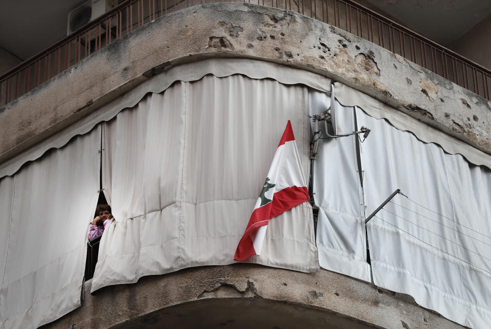 A Lebanese woman stands on her apartment balcony that is still riddled with bullets left over from the 1975-1990 Lebanese civil war on a former Beirut frontline between Christian district of Ain el-Rummaneh and a Muslim Shiite district of Shiyah, as he watches a protest against the return of the civil war, in Beirut, Lebanon, Wednesday, Nov. 27, 2019. Hundreds of Lebanese women marched across a former front line in the Lebanese capital carrying white roses and Lebanese flags to denounce overnight clashes between rival groups that injured dozens of people. (AP Photo/Hussein Malla)