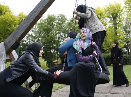 Yasmin (L), 16, pushes Hana (C), 16, on a swing after finishing a GCSE exam near their school in Hackney, east London June 6, 2013. REUTERS/Olivia Harris