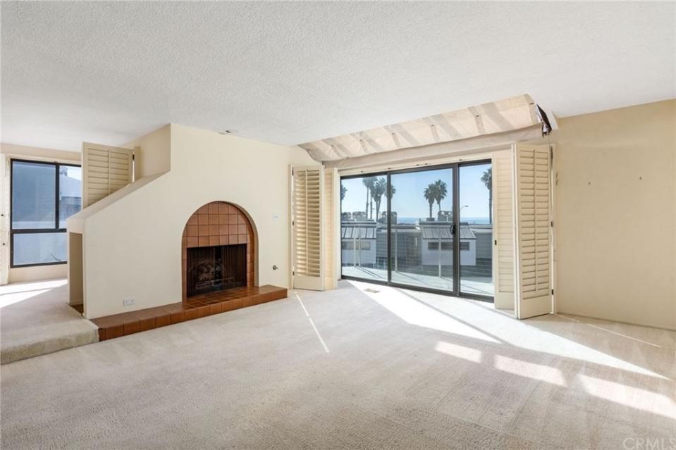 An empty living room with cream carpeted flooring and a terracotta tiled fireplace