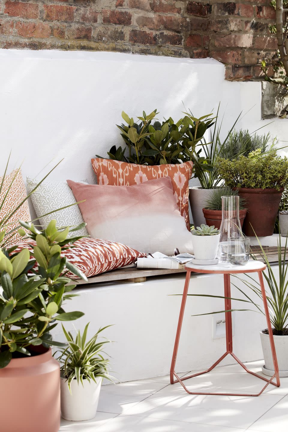 outside seating area, brickwork painted white, potted plants surrounded the seat with pink and rose gold cushions scattered