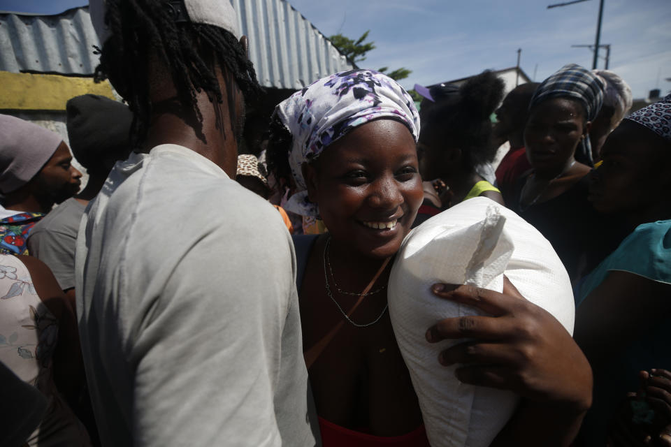 A woman smiles as she leaves carrying a sac of rice, from a government distribution of food and school supplies at the mayor's office in Cite Soleil, Port-au-Prince, Haiti, Thursday, Oct. 3, 2019. The administration of President Jovenel Moise tried to alleviate Haiti’s economic crunch on Thursday by distributing plates of rice and beans, sacks of rice, and school backpacks filled with four notebooks and two pens. (AP Photo/Rebecca Blackwell)