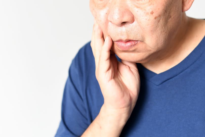 An elderly Asian man with a troubled face holding his cheeks.