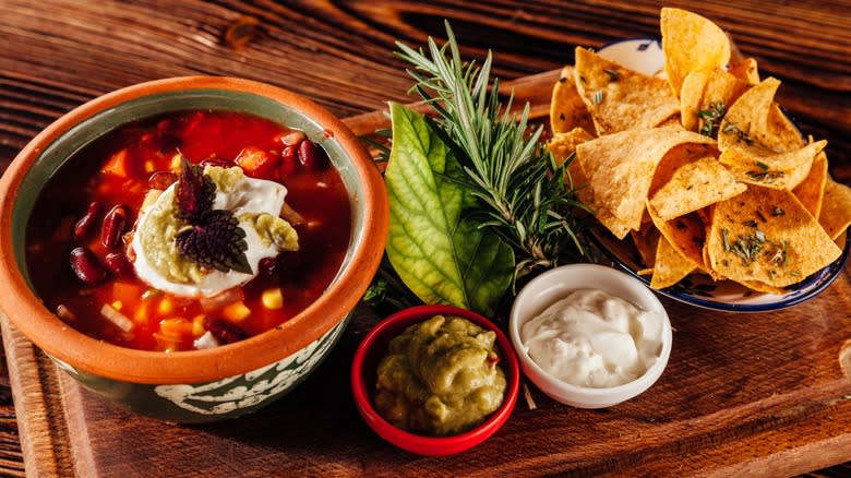 A bowl of soup, tortilla chips, and some condiments