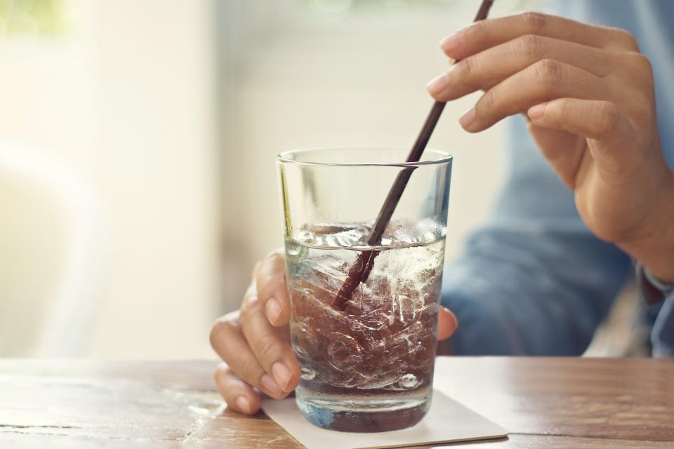 Person holding a glass with a straw, resting on a table beside a window