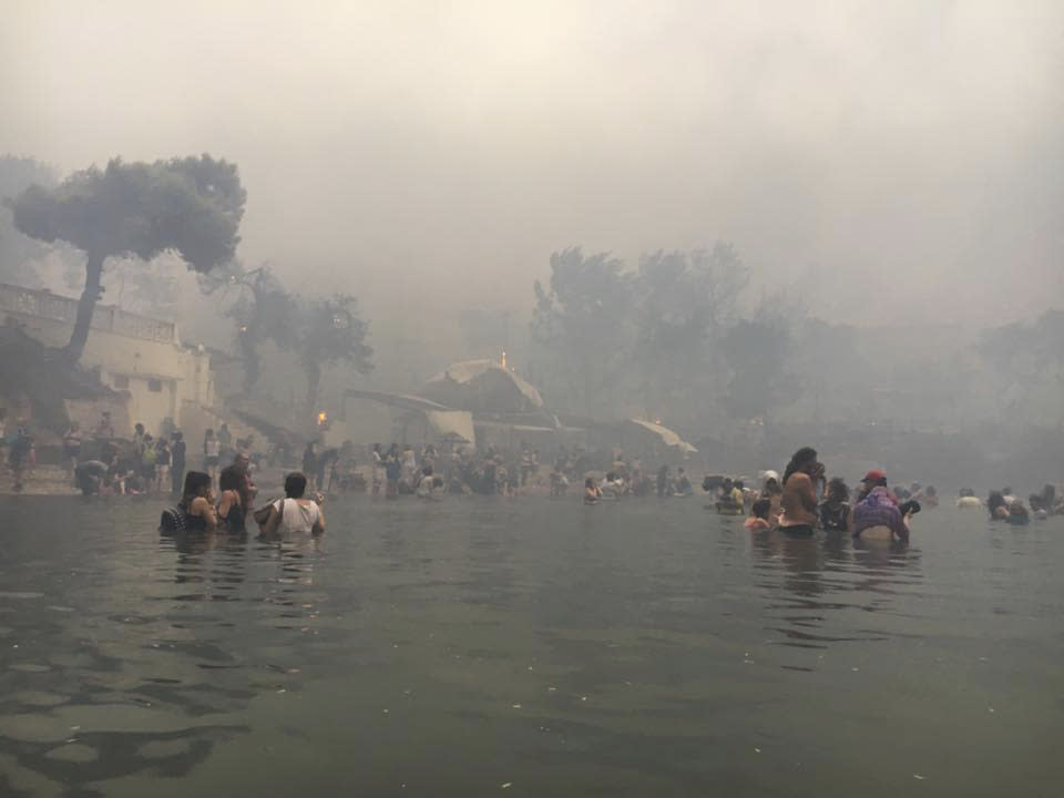 In this Monday, July 23, 2018 image from video provided by Elia Kallia, people escaping wildfires wade into the waters of the "Silver Coast" beach in Mati, Greece. Dozens were either killed by flames or drowned as they tried to flee the fire into the nearby sea, waiting for hours in the water for rescue from local fishermen and other boat owners. (Elia Kallia via AP)