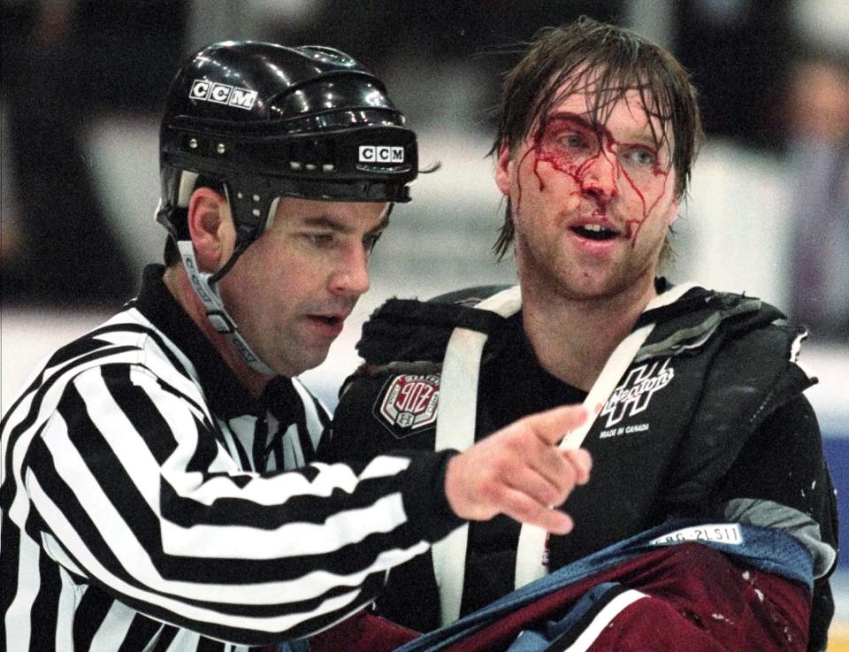 Linesman Dan Schachte leads a bleeding Colorado Avalanche goaltender Patrick Roy to his bench after Roy was involved in a fight with Detroit Red Wings' goaltender Mike Vernon in Detroit on March 26, 1997.