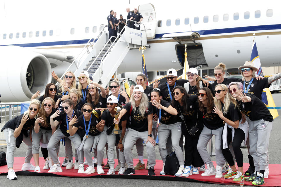 Members of the United States women's soccer team, winners of a fourth Women's World Cup, pose with the trophy by their plane after arriving at Newark Liberty International Airport, Monday, July 8, 2019, in Newark, N.J. Julie Ertz holds the trophy, Megan Rapinoe, front right, gestures, and Alex Morgan, back left, also gestures. (AP Photo/Kathy Willens)