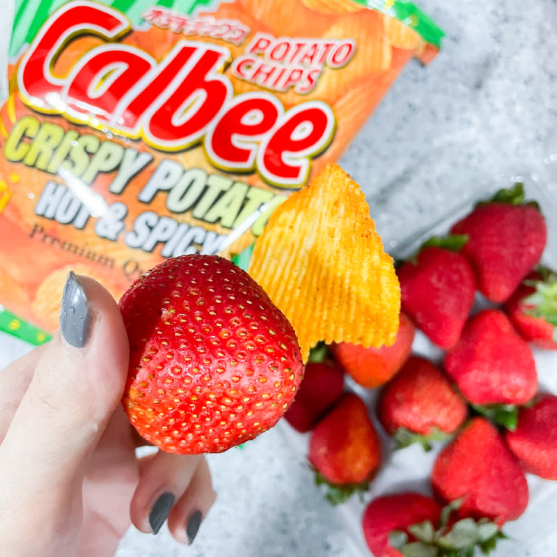 a hand in frame shot of strawberries and potato chips