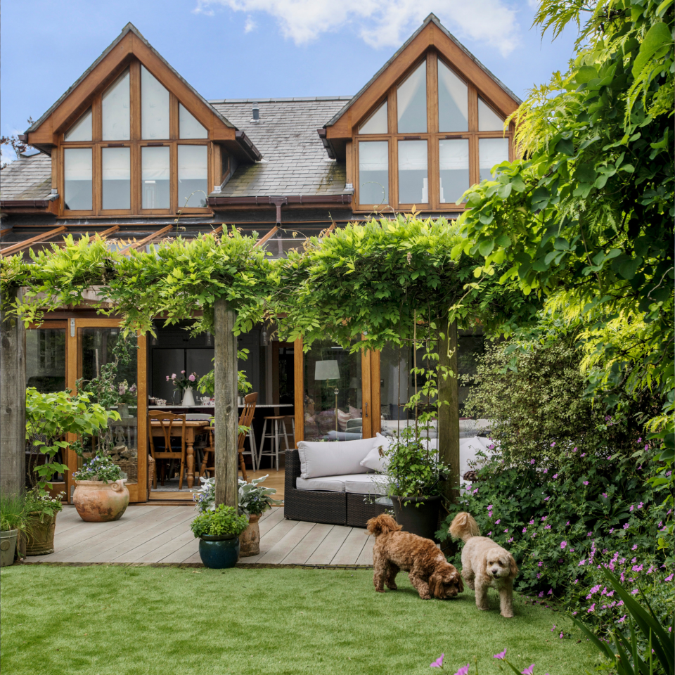 Exterior of the detached 5 bed house taken from the garden with the decked area under the glass awning and the lawn. A renovated and extended 1930s two bedroom bungalow, extended to a five bedroom family home, then renovated a second time after a fire, home of Amanda Arkell, interior designer, her husband Steve, family and two pets in Christchurch, Dorset.