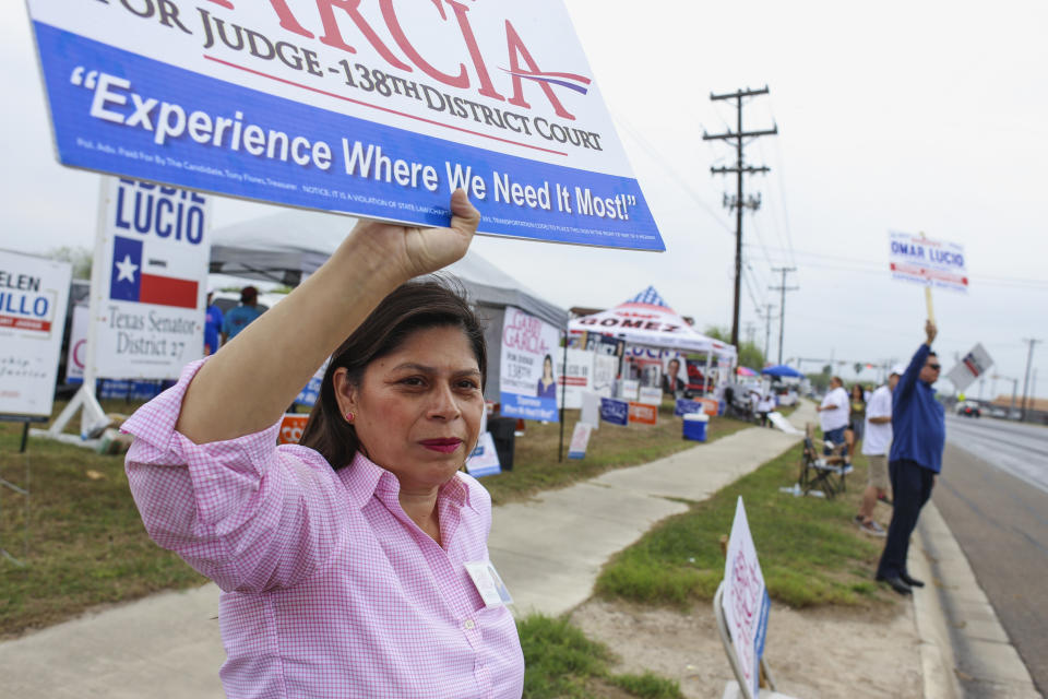 Gabriela Garcia holds one of her campaign signs as she greets passing cars during her campaign for judge in the 138th state District Court Tuesday, March 3, 2020, outside the polling location at Burns Elementary School in Brownsville, Texas. (Denise Cathey/The Brownsville Herald via AP)