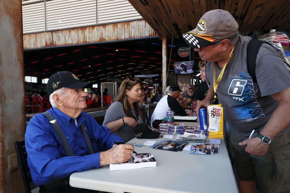 Former NASCAR driver Bobby Allison, left, signs autographs in Big Bill's Garage before the NASCAR Cup Series auto race Sunday, Oct. 2, 2022, in Talladega, Ala. (AP Photo/Butch Dill)
