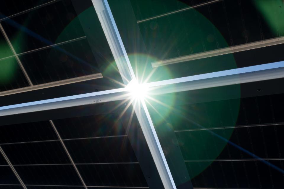 Sunlight peeks through the gaps in a solar array as workers from Good Energy Solutions install a solar site in Topeka, Kansas, Nov. 1, 2023.