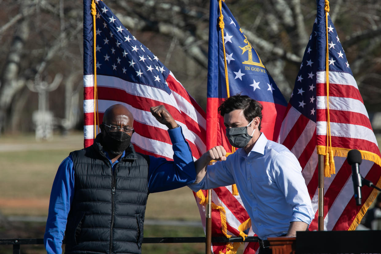 Democratic U.S. Senate candidates Raphael Warnock (L) and Jon Ossoff bump elbows during an outdoor drive-in rally on December 5, 2020 in Conyers, Georgia. (Photo by Jessica McGowan/Getty Images) 