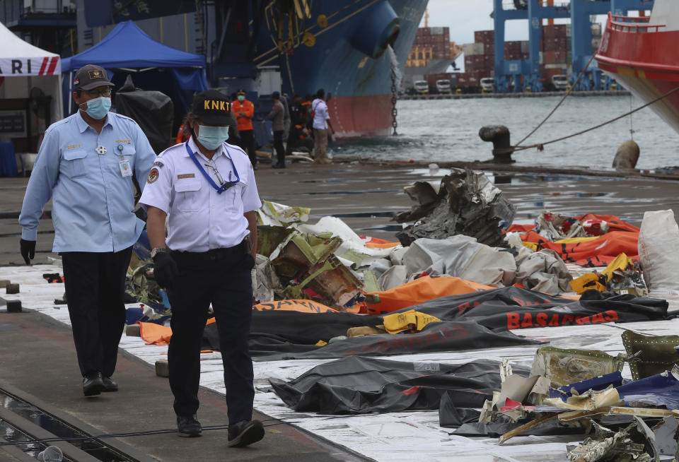 Indonesian National Transportation Safety Committee (KNKT) investigators walk near debris found in the waters around the location where a Sriwijaya Air passenger jet crashed, at the search and rescue command center at Tanjung Priok Port in Jakarta, Indonesia, Indonesia, Wednesday, Jan. 13, 2021. Divers looking for the crashed plane's cockpit voice recorder were searching in mud and plane debris on the seabed between Indonesian islands Wednesday to retrieve information key to learning why the Sriwijaya Air jet nosedived into the water over the weekend. (AP Photo/Achmad Ibrahim)