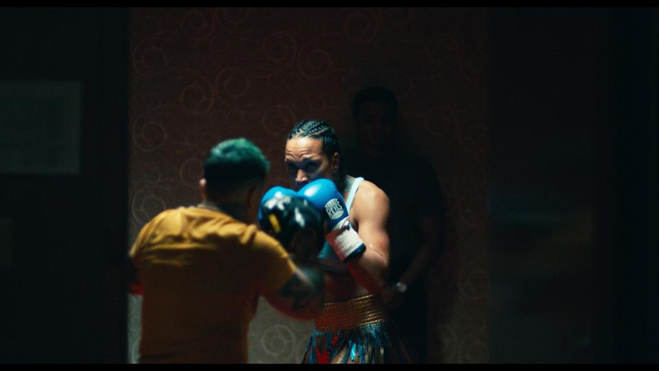 A woman holds up her hands in boxing gloves as she faces a sparring partner.