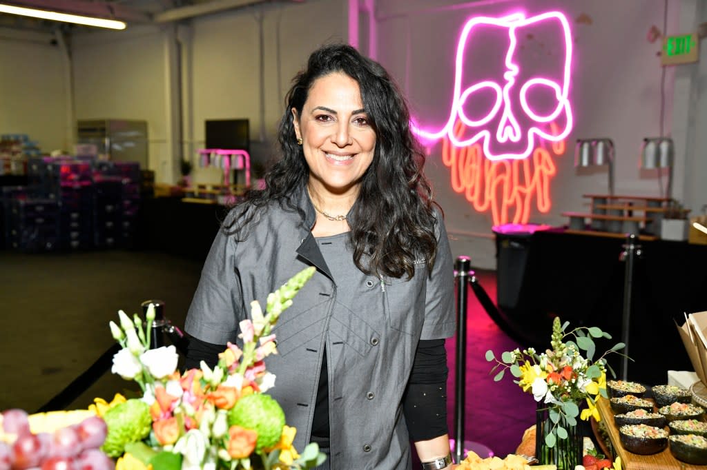 Chef Penny Davidi in a grey chef's jacket standing in front of a platter of food