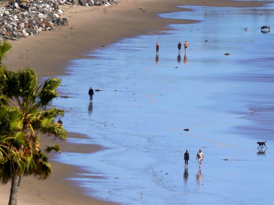 People walk along the beach from a distance during low tide in Malibu, California