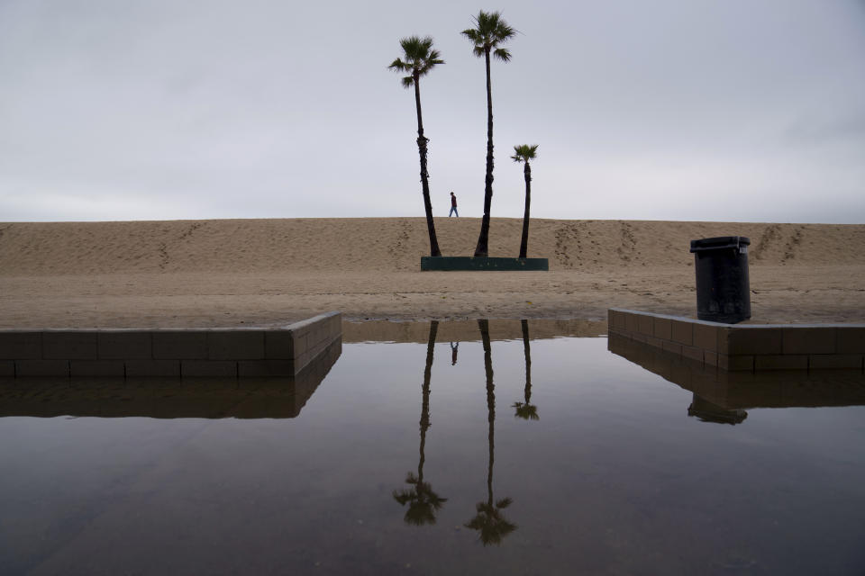 A person walks along the beach with flooding along the boardwalk Thursday, Feb. 1, 2024 in Seal Beach, Calif. (AP Photo/Eric Thayer)