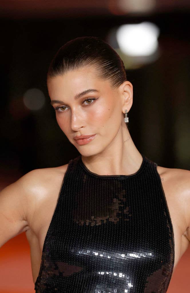 Hailey Bieber poses on the red carpet in a sleeveless, black, sequin dress with sleeked-back hair