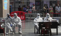 Health workers take a break from taking nasal swab samples from passengers to test for for COVID-19 at a train station in Mumbai, India, Friday, Nov. 27, 2020. India has more than 9 million cases of coronavirus, second behind the United States. (AP Photo/Rafiq Maqbool)