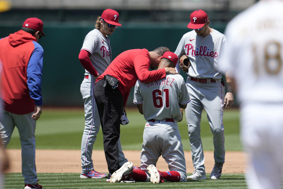 Philadelphia Phillies pitcher Cristopher Sánchez (61) is checked on by a trainer and teammates after being hit by a base hit by Oakland Athletics' Esteury Ruiz during the fourth inning of a baseball game in Oakland, Calif., Saturday, June 17, 2023. (AP Photo/Jeff Chiu)