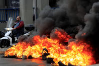 A man rides his scooter past burning tires at one of main roads during a protest against the increase in prices of consumer goods and the crash of the local currency, in Beirut, Lebanon, Monday, Nov. 29, 2021. (AP Photo/Hussein Malla)
