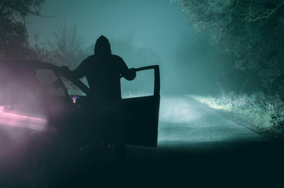 a silhouette of a person standing outside of their car in the middle of a dark road