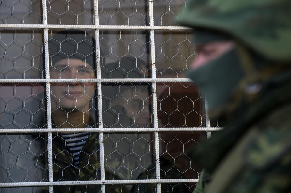 A Ukrainian Navy sailor smiles as he looks out of a window near the entrance to the General Staff Headquarters of the Ukrainian Navy, as an unidentified soldier stands outside in Sevastopol, Monday, March 3, 2014. (AP Photo/Andrew Lubimov)