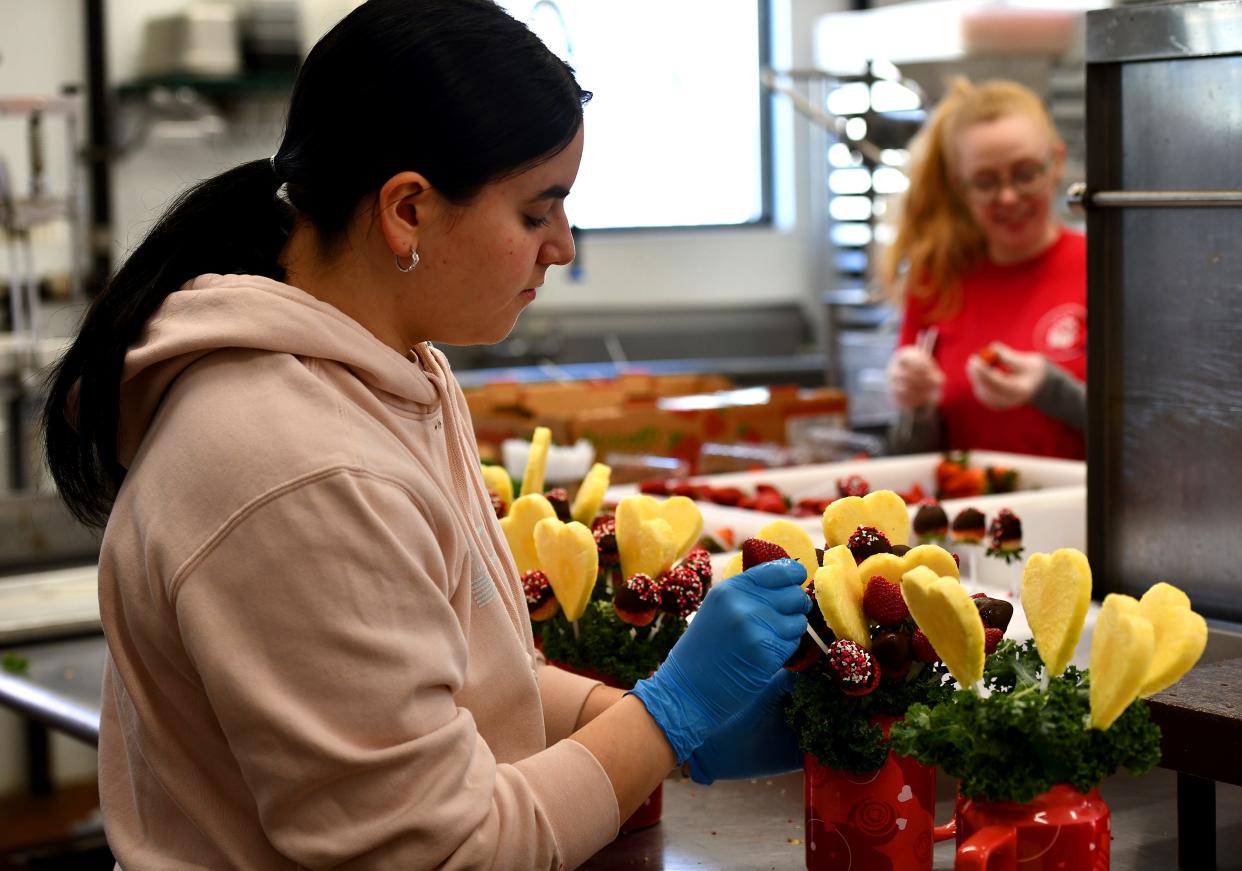 WORCESTER - Edible employee Lily Callahan of Fitchburg adds pineapple hearts and strawberries dipped in chocolate to an arrangement for Valentine's Day. The Pleasant Street business was very busy on the holiday.