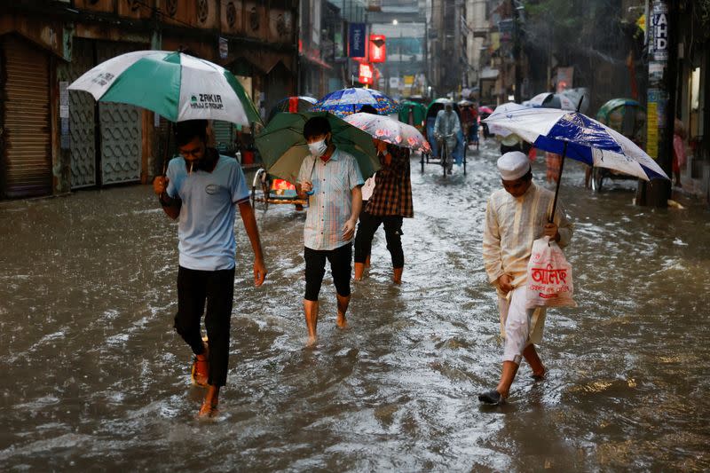 People wade through a flooded street, amid continuous rain before the Cyclone Sitrang hits in Dhaka