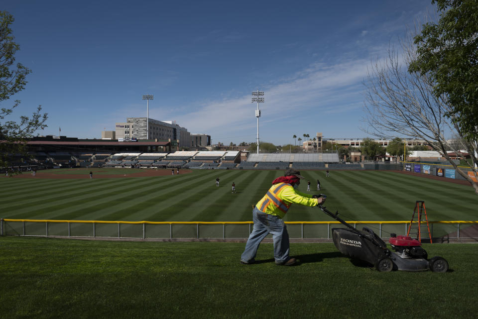 A worker mows the lawn at Scottsdale Stadium as San Francisco Giants players take part in a drill during the team's spring training baseball workout in Scottsdale, Ariz., Friday, Feb. 26, 2021. (AP Photo/Jae C. Hong)