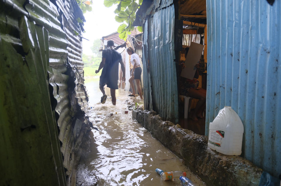 People walk between houses flooded by the rains of Tropical Storm Franklin, along the Ozama River in the Gualey neighborhood of Santo Domingo, Dominican Republic, Wednesday, Aug. 23, 2023. (AP Photo/Ricardo Hernandez)